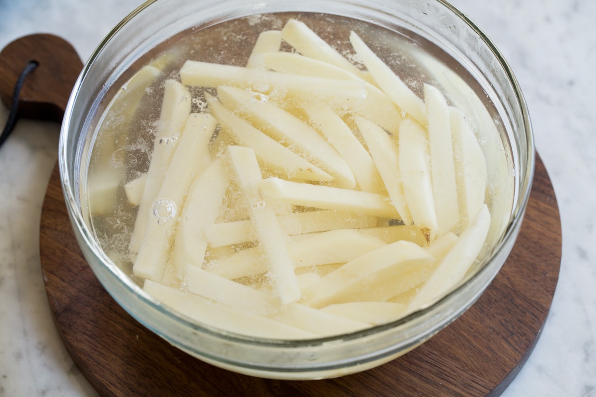 Soaking potato sticks in a glass bowl full of water to remove excess starches.