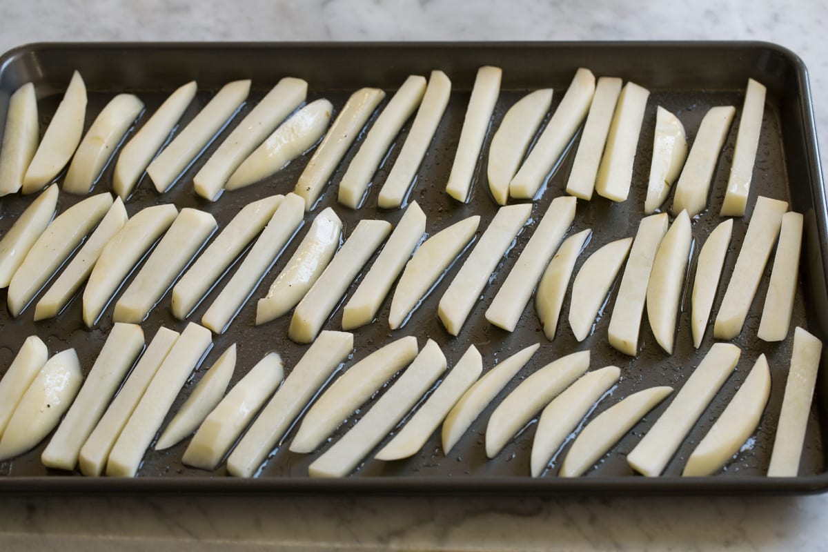 Spreading cut fries onto baking sheet with oil.