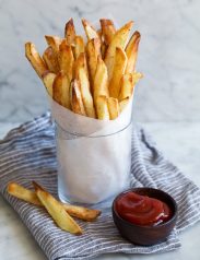 Cup full of french fries in parchment paper with a side of ketchup.