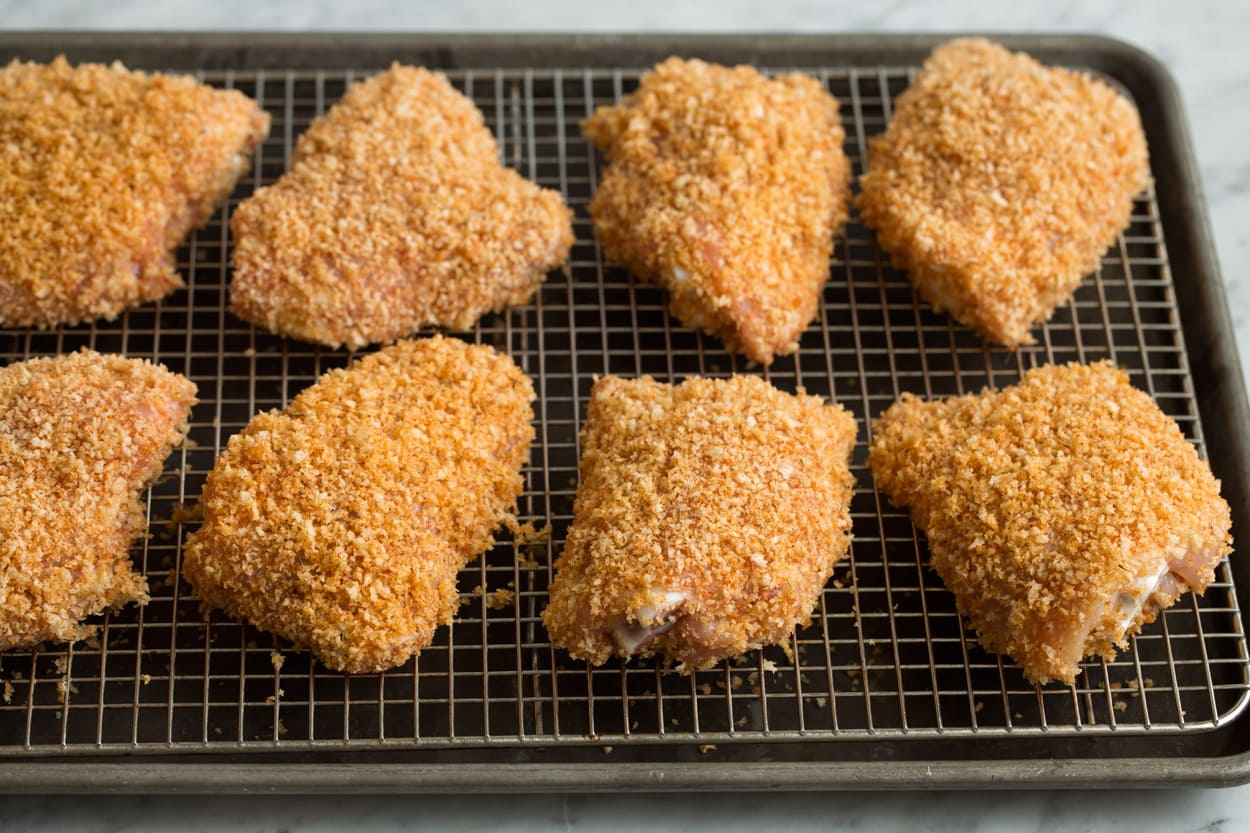 Eight panko and olive oil coated chicken thighs on a wire cooling rack set over a baking sheet before baking.