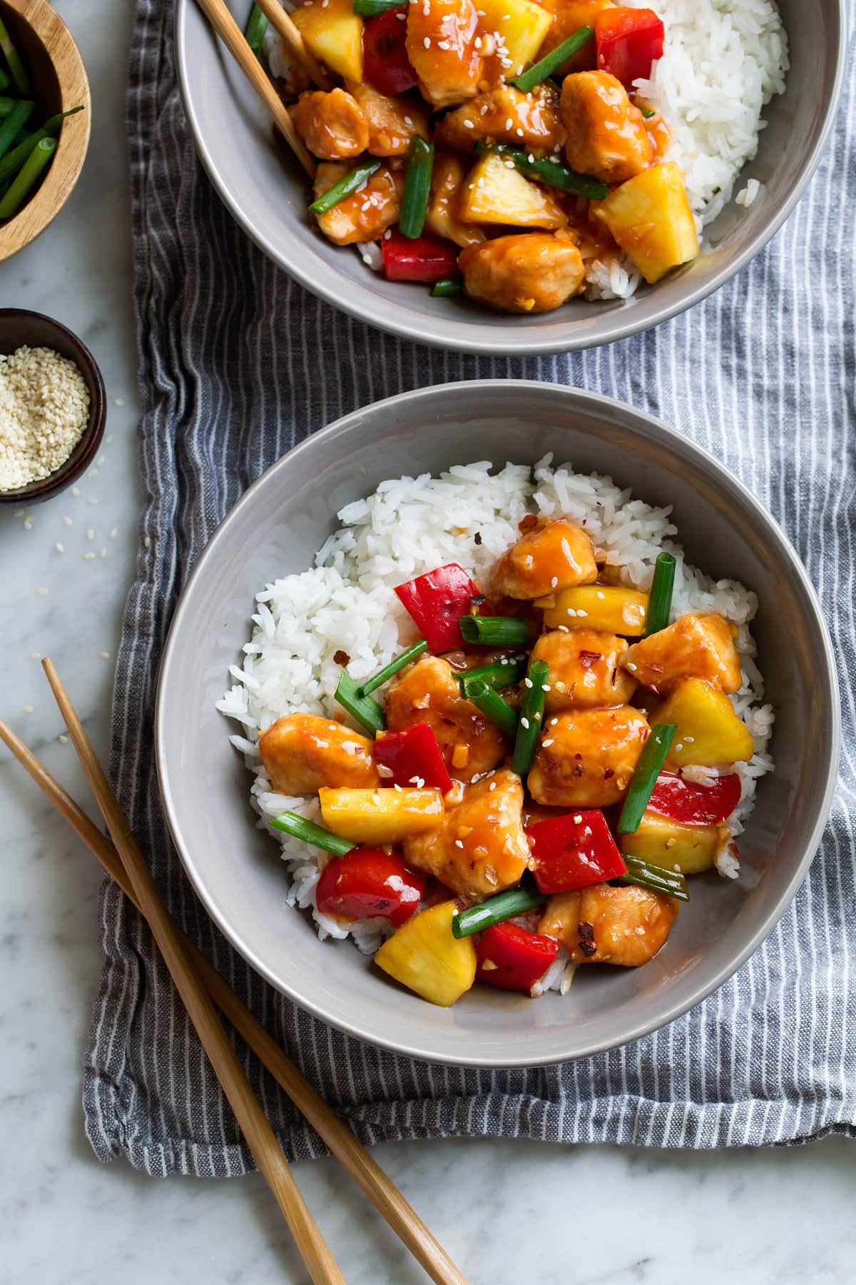 Two servings of sweet and sour chicken over white rice grey serving bowls.