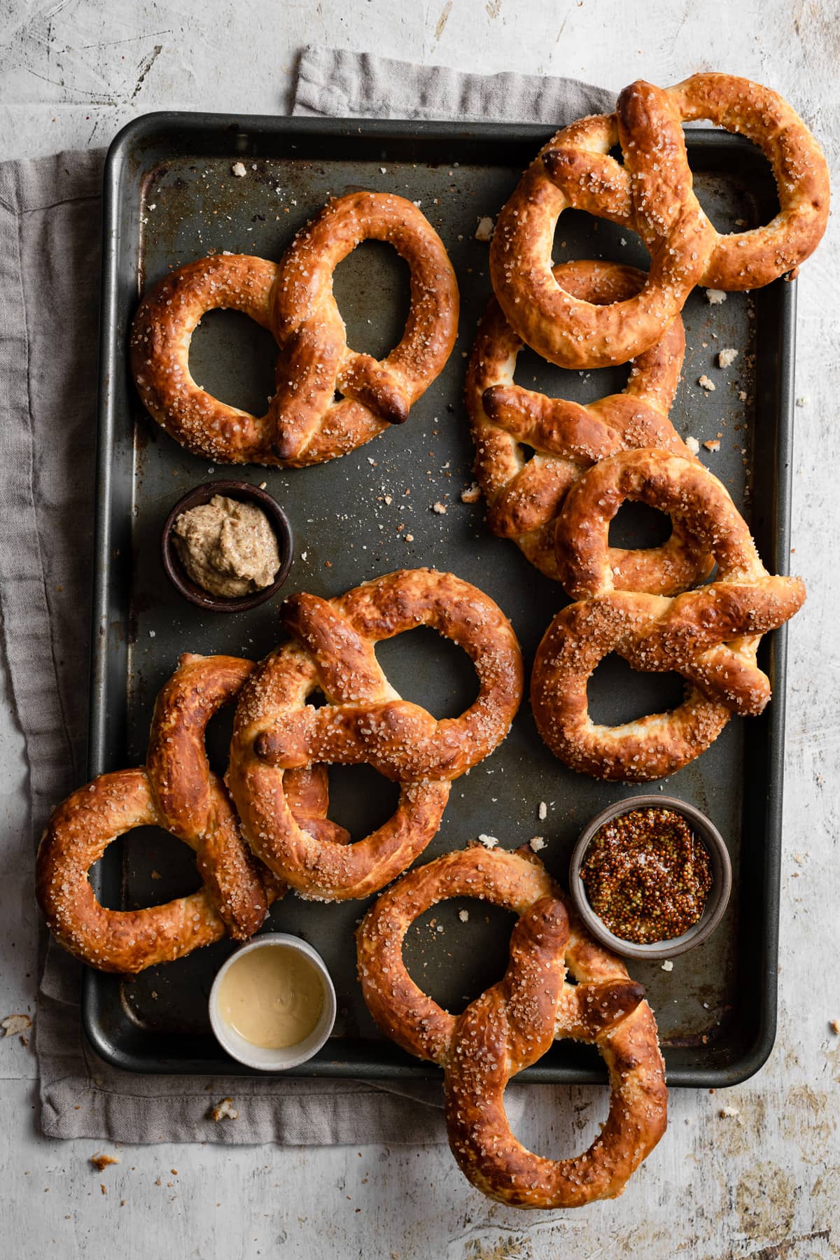 Overhead image of seven soft pretzels on a dark baking sheet.