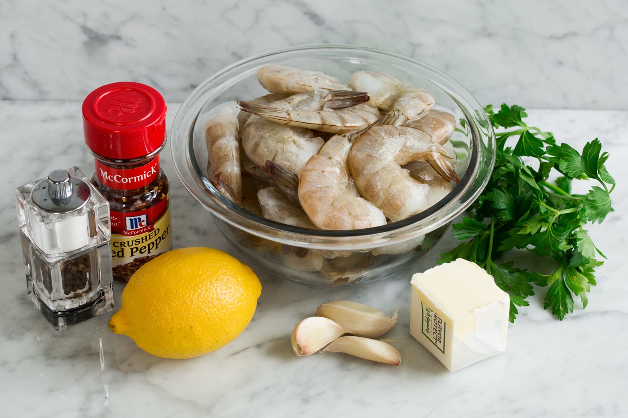 Ingredients needed to make baked shrimp shown here, including raw shrimp, butter, garlic, lemon, parsley, red pepper flakes, salt and pepper.