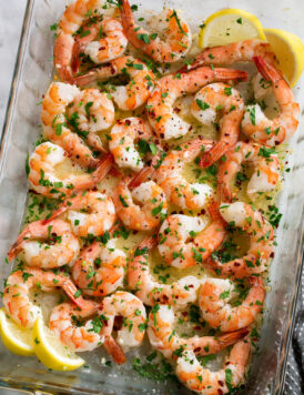 Overhead image of baked shrimp with lemon butter sauce in baking dish.