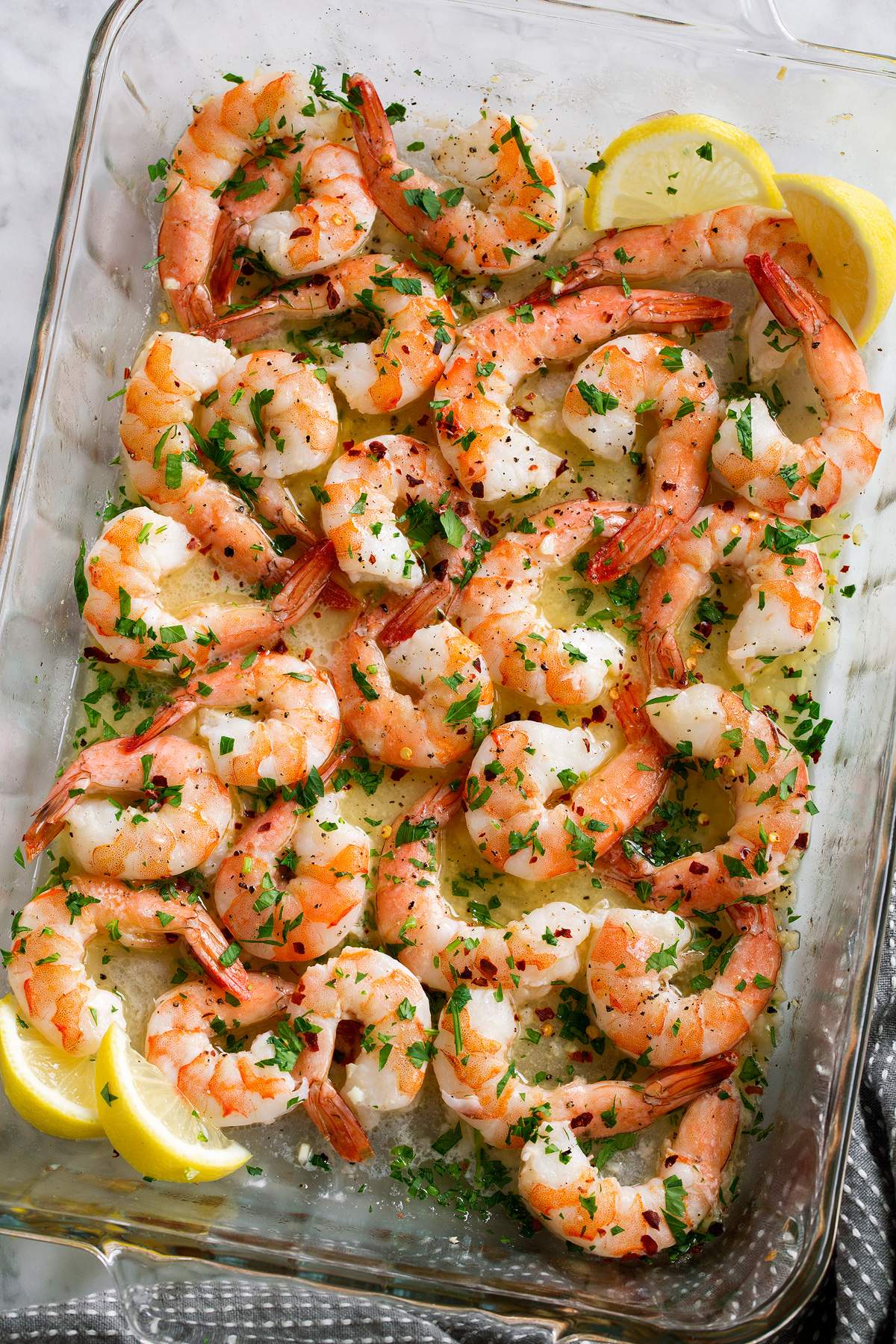Overhead image of baked shrimp with lemon butter sauce in baking dish.
