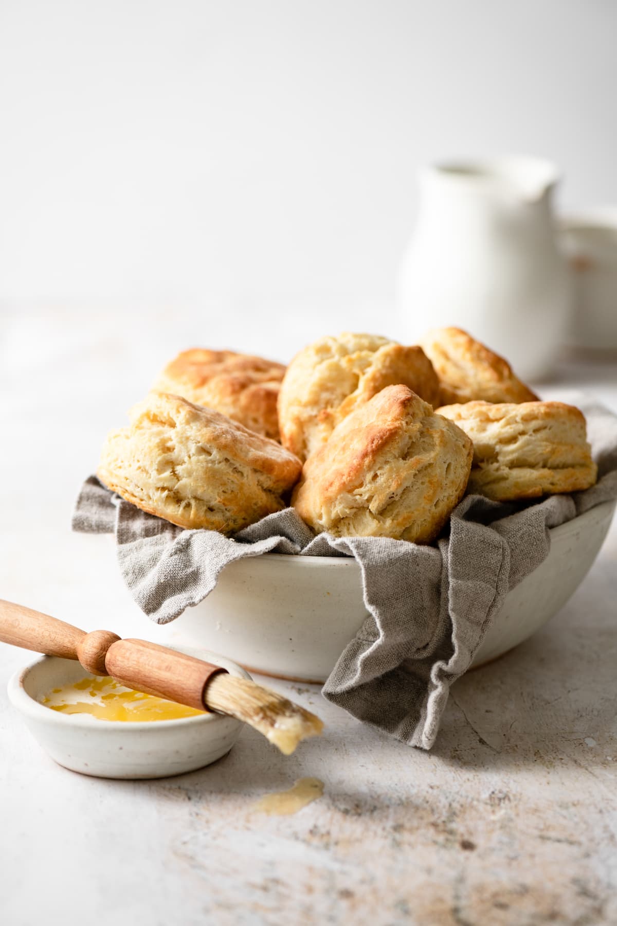 Bowl full of buttermilk biscuits with a pastry brush and butter on the side. 