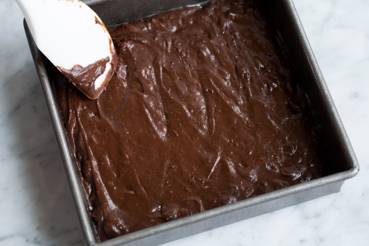 Spreading brownie batter into an aluminum 8 by 8-inch baking dish.