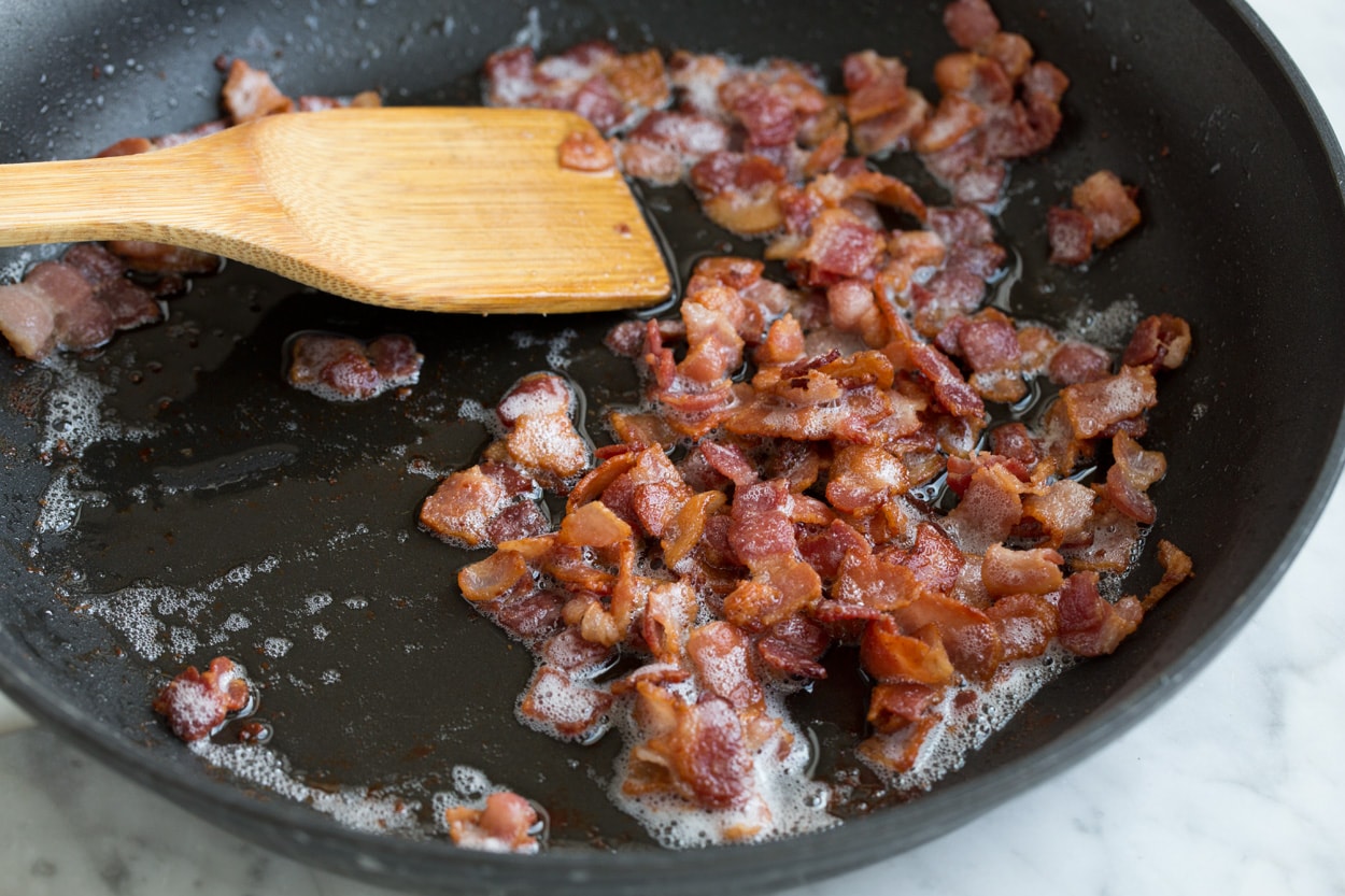 Sauteeing bacon in a large black skillet to make a frittata.
