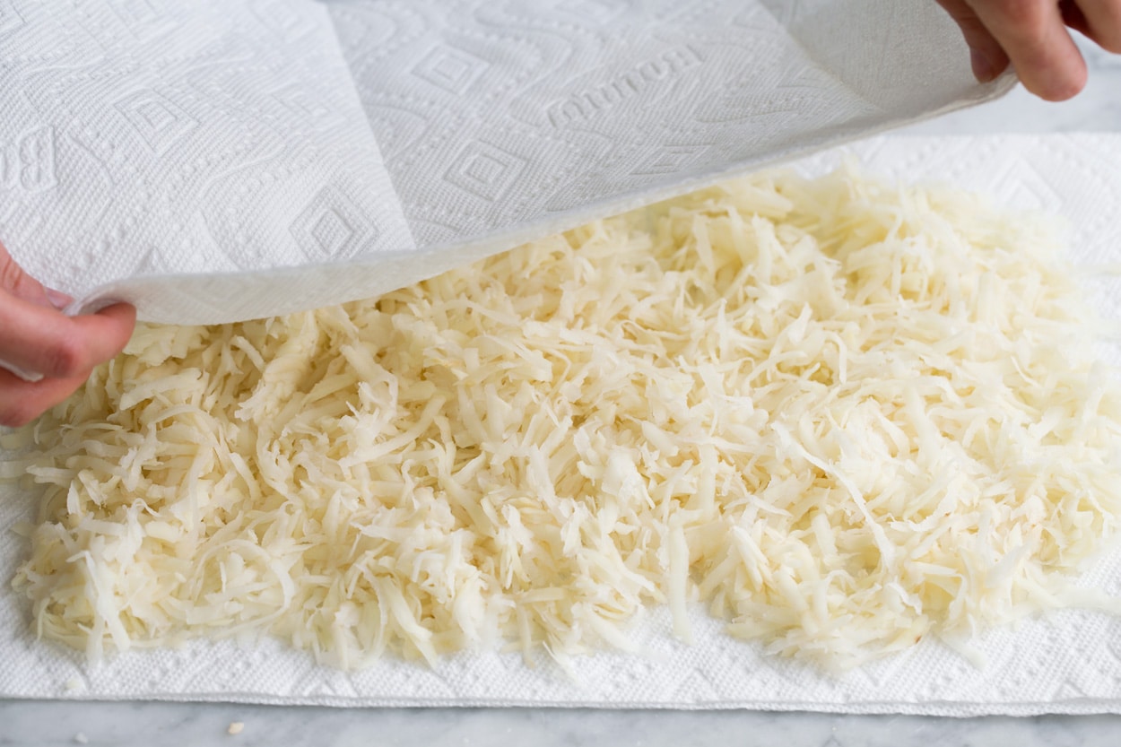 Shredded potatoes layered over paper towel and covering with more paper towels to press out excess liquid.