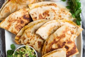 Overhead image of 8 quesadilla wedges on a white oblong platter served with pico and guacamole.