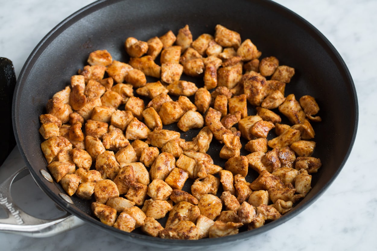 Sautéing spiced chicken cubes in a large black skillet for quesadillas.