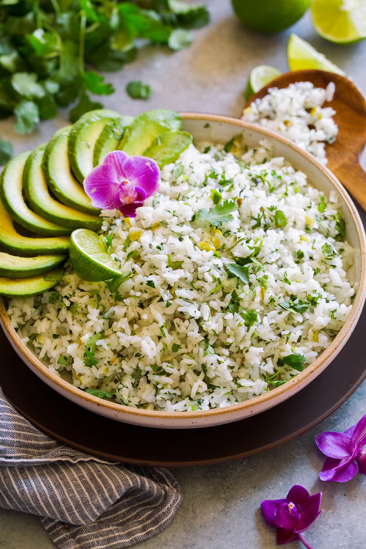 Serving bowl full of cilantro lime rice garnished with avocado slices, cilantro leaves, orchid flower and lime. 