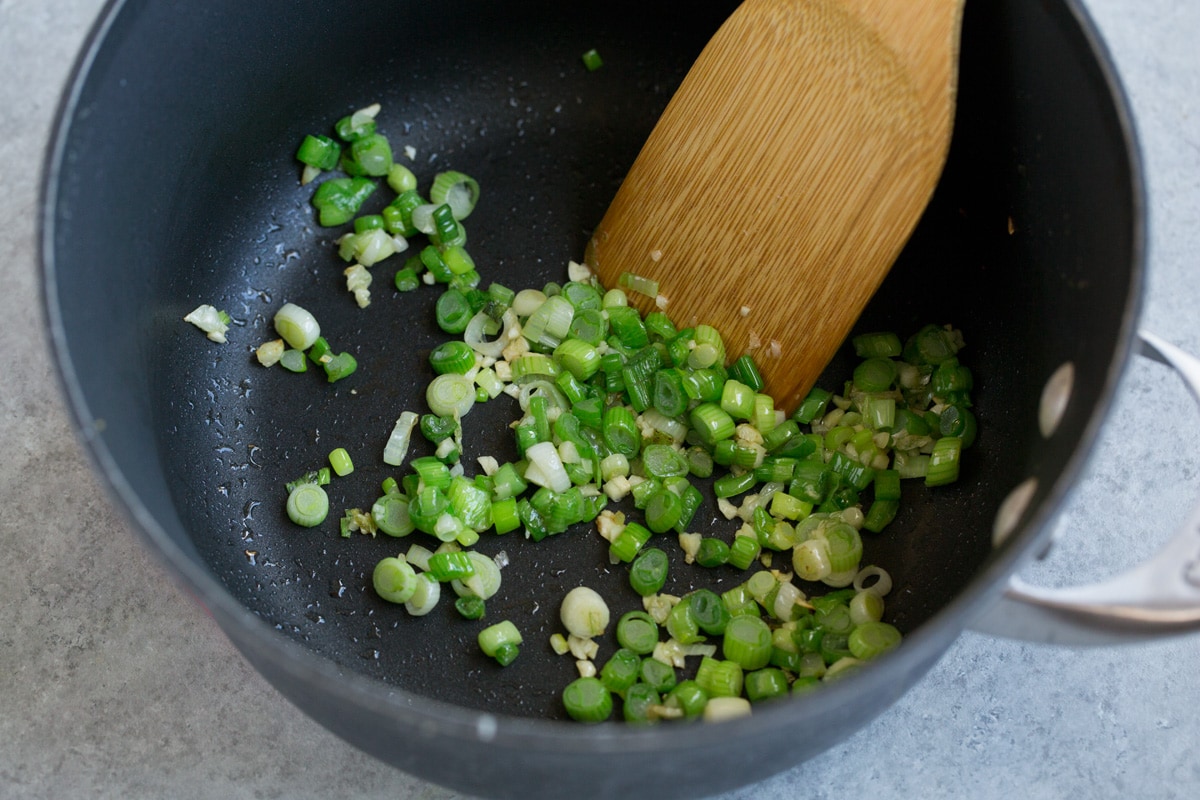Showing how to make cilantro lime rice, starting by sauteing green onion and garlic in a saucepan. 