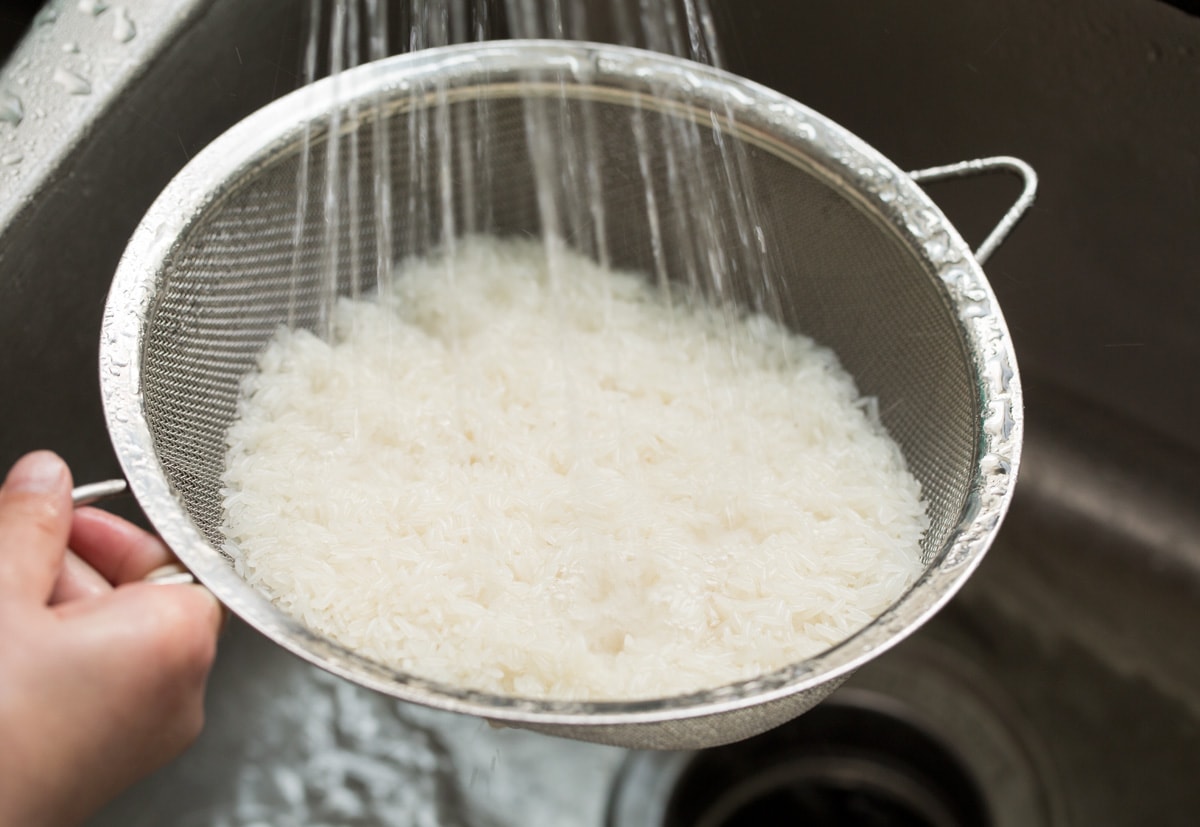Showing how to make coconut rice. Starting by rinsing rise under water in a fine mesh sieve.