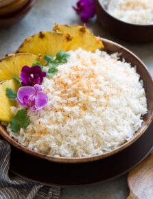 Coconut rice in a wooden bowl set over a brown plate on a grey surface.