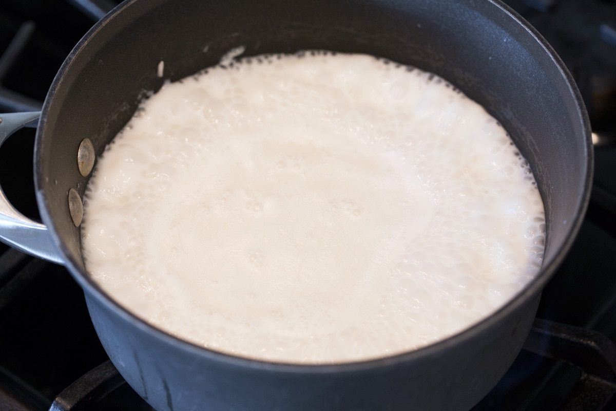 Bringing coconut milk and rice mixture to a boil in saucepan over stovetop.
