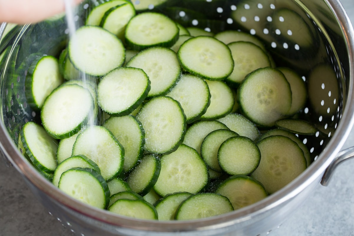 Showing how to make cucumber salad. Tossing cucumbers in a colander with salt.
