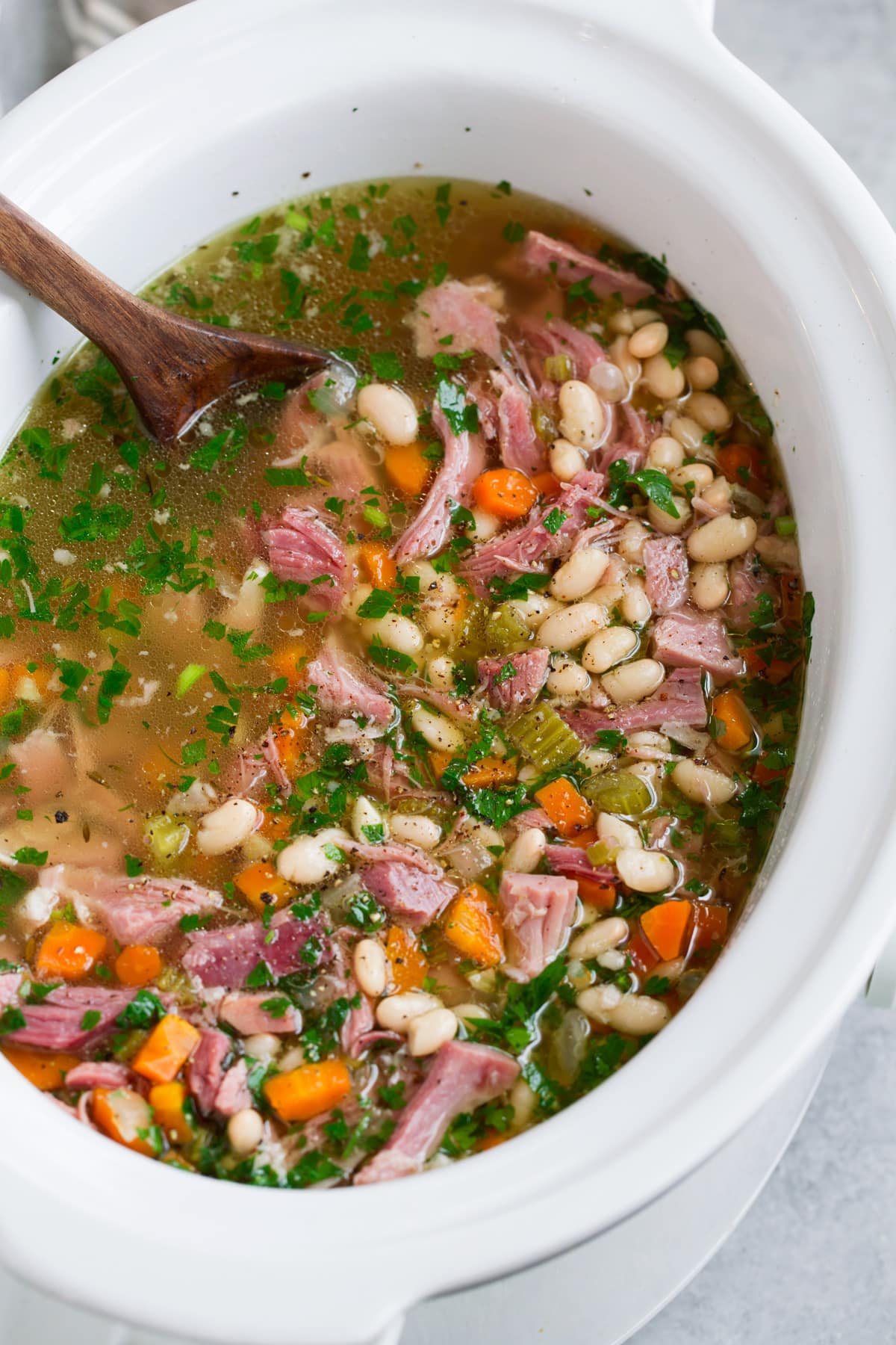 Ham and bean soup shown in a white slow cooker after cooking.