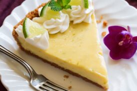 Slice of Best Key Lime Pie on white scalloped dessert plate set over a maroon napkin.