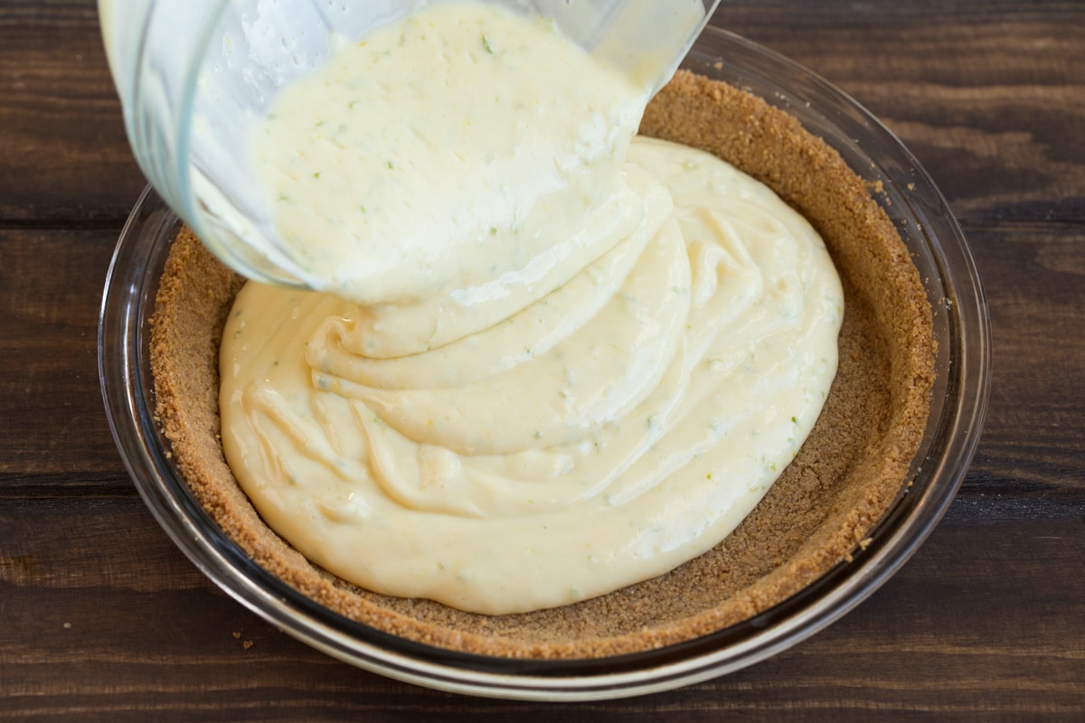 Pouring key lime pie filling over crust in glass pie pan.