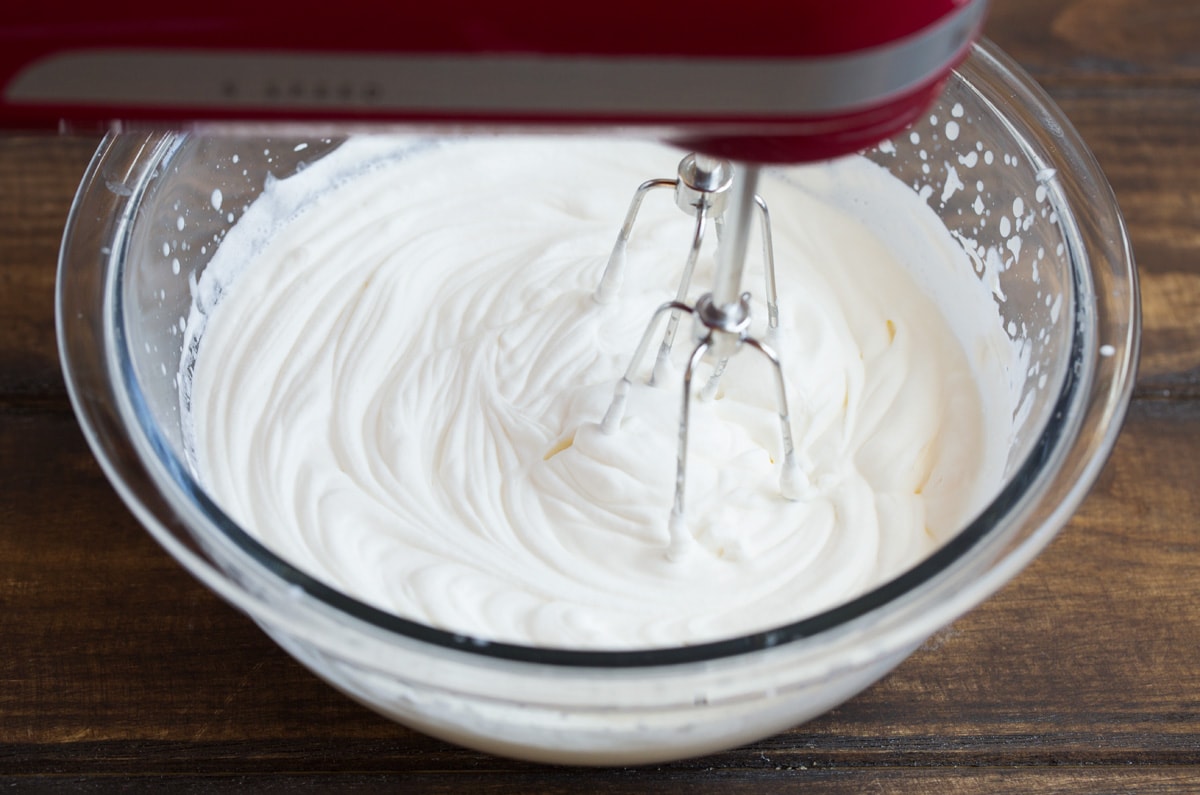 Making whipped cream topping in a glass mixing bowl using an electric hand mixer. Topping is for key lime pie.