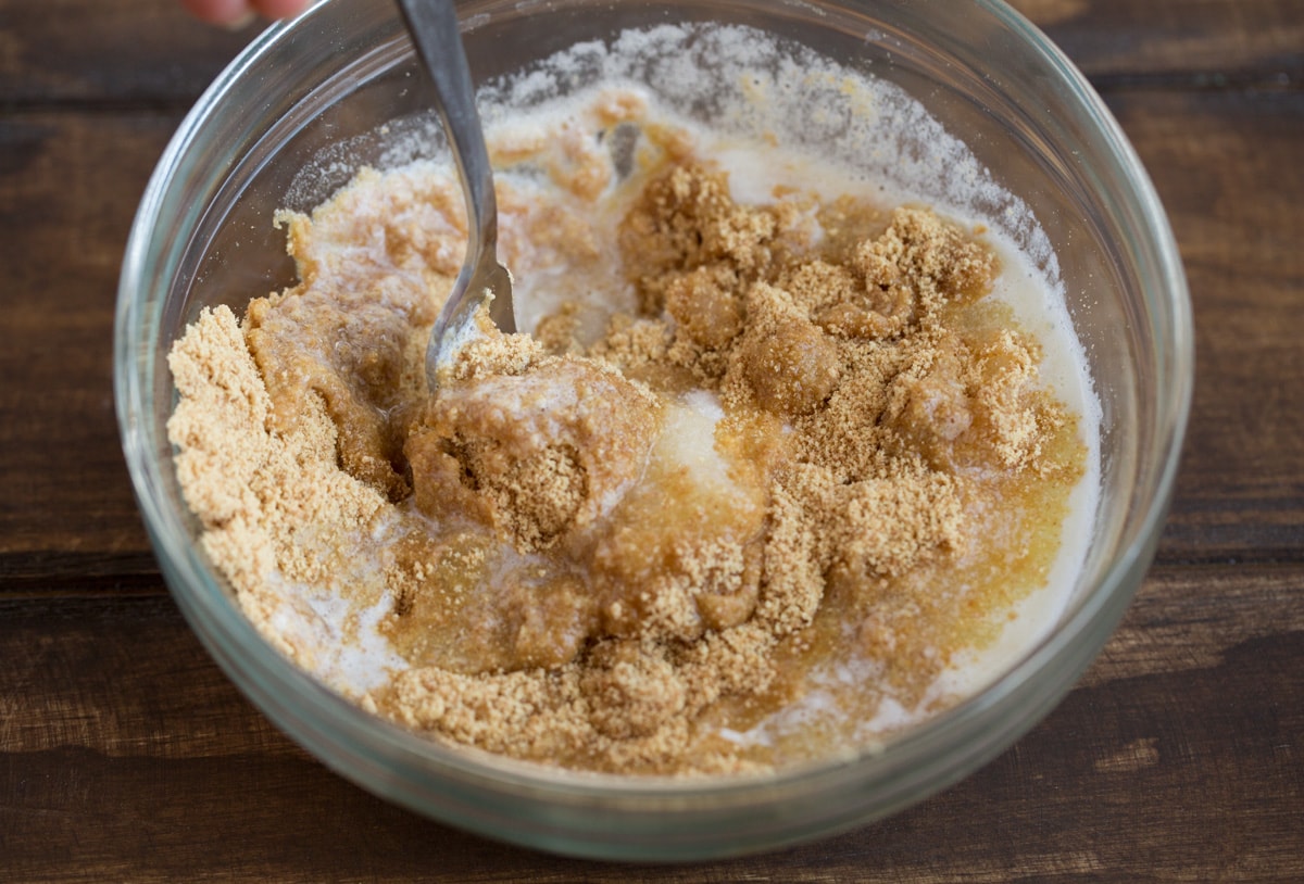 Showing how to make graham cracker crust for key lime pie. Stirring together graham cracker crumbs, butter and sugar in a glass mixing bowl.