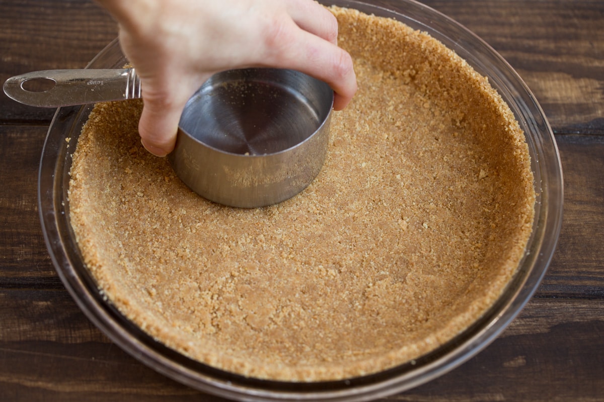 Pressing graham cracker crumbs into a 9-inch glass pie dish for key lime pie base.