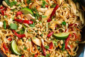 Pad Thai in a black wok with chicken and fresh vegetables.