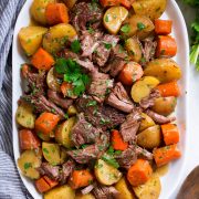 Slow Cooker Pot Roast with potatoes and carrots on a white oval serving platter set over marble.