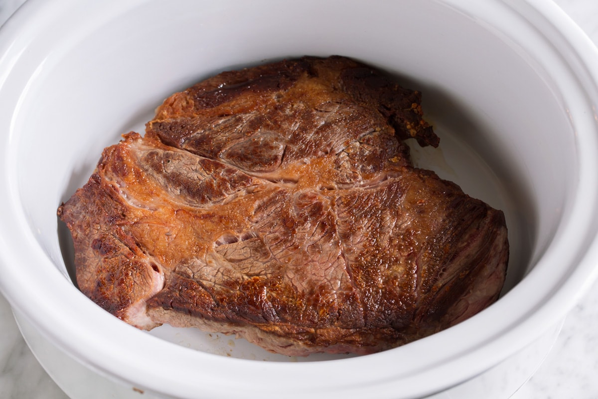 Showing how to make crockpot pot pot roast, placing scorched chuck roast in a slow cooker.