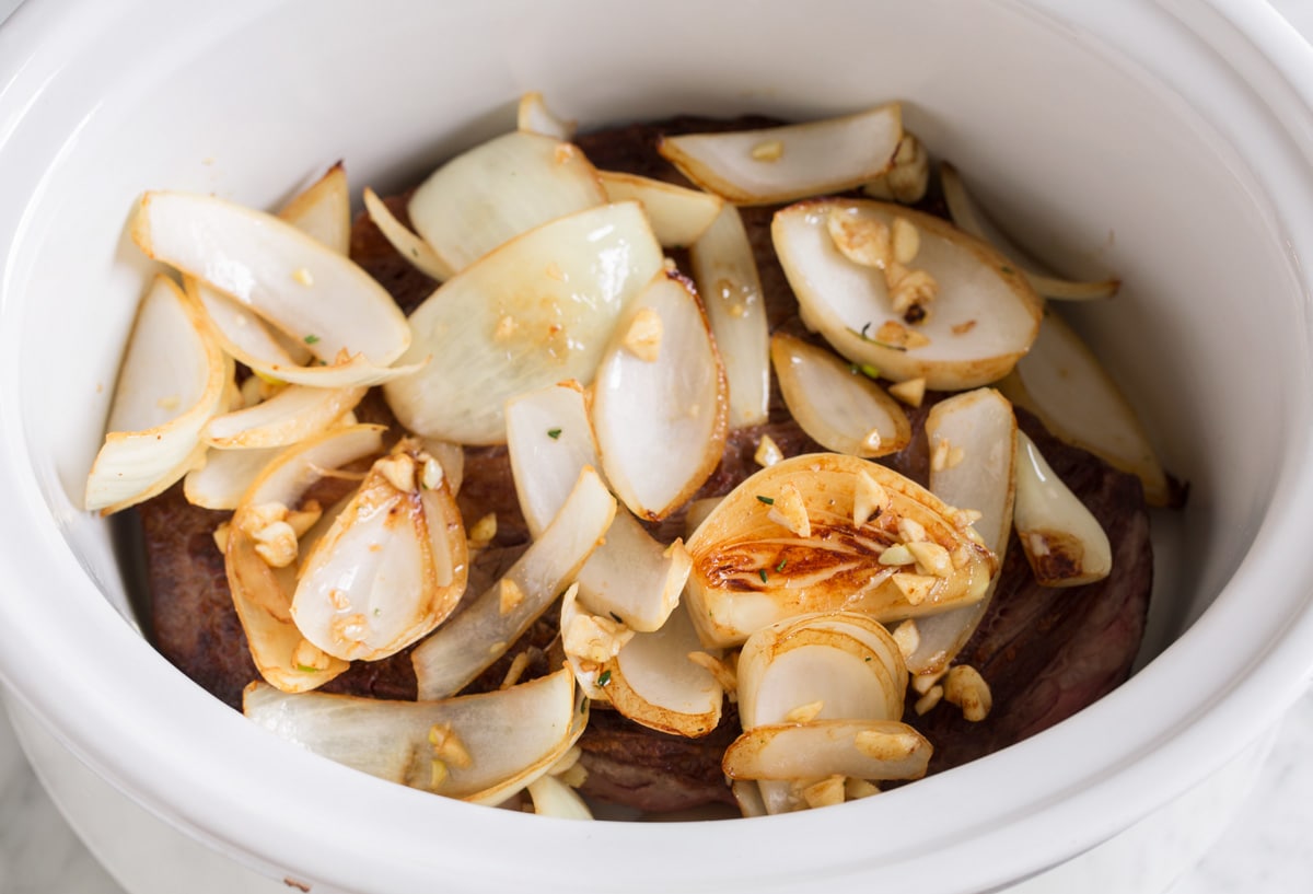 Add sautéed onions and garlic over the chuck roast in slow cooker.