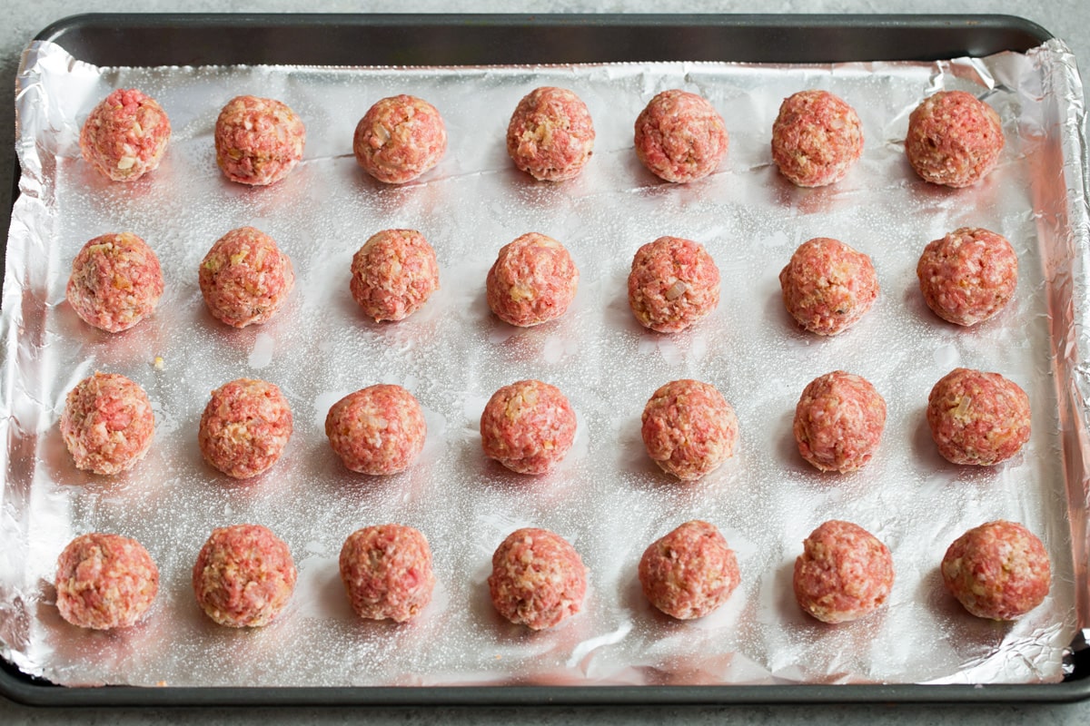28 shaped Swedish meatballs on foil lined baking sheet, shown before baking.