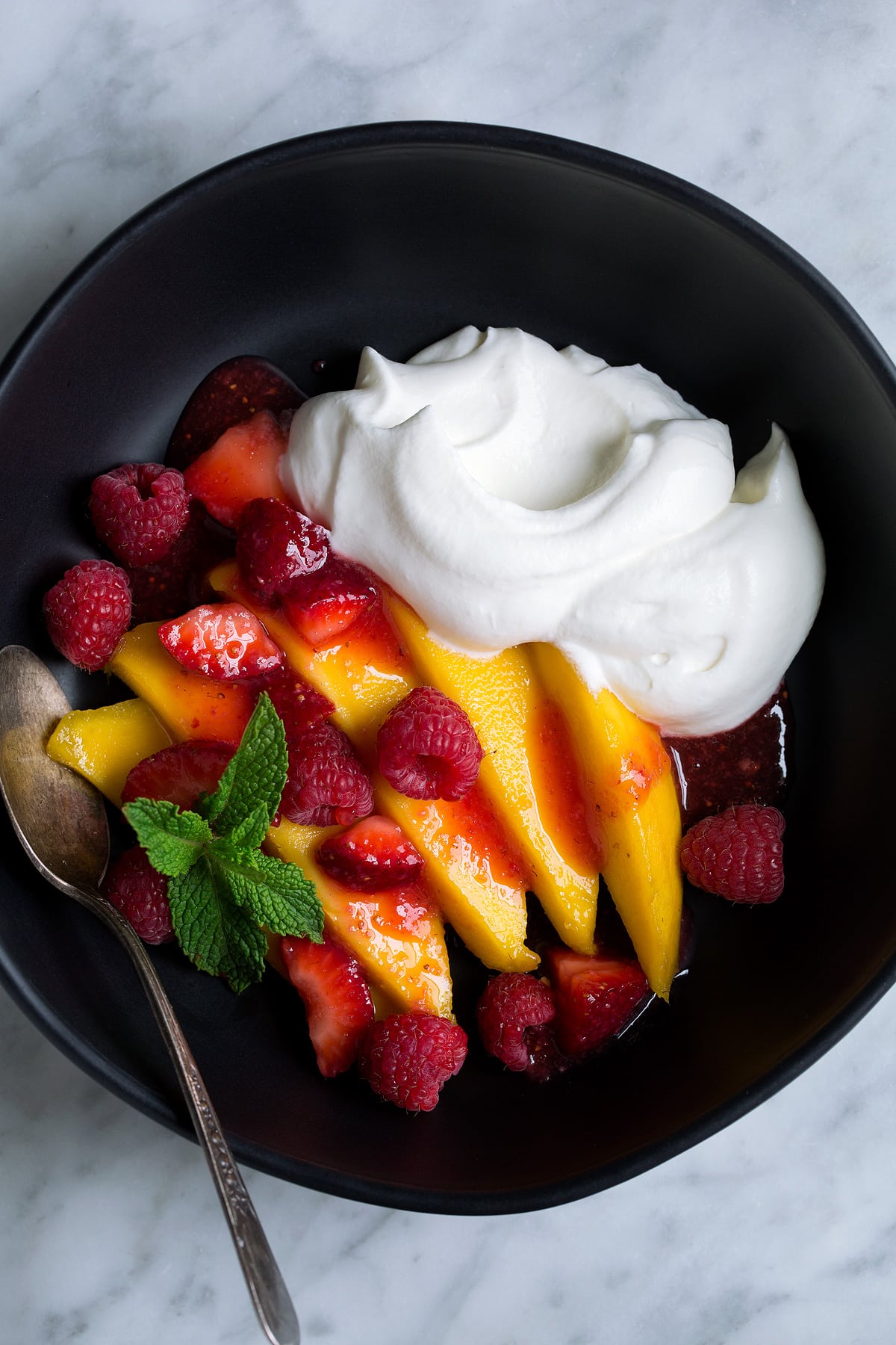 Whipped Cream served with fresh mangoes, strawberries and raspberries in a black bowl.