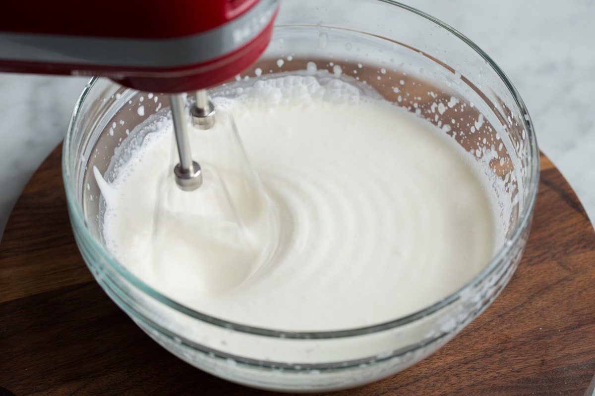 Showing how to make whipped cream. Mixing heavy cream and sugar in a glass mixing bowl using an electric hand mixer until thickened.