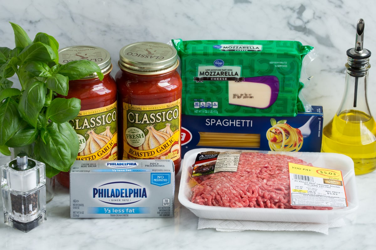 Baked spaghetti ingredients shown here including spaghetti, ground beef, marinara sauce, light cream cheese, fresh basil, mozzarella and olive oil.
