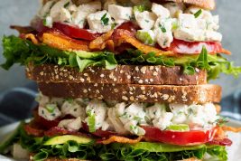 Stack of two chicken salad sandwiches on a white plate set over a dark grey cloth.