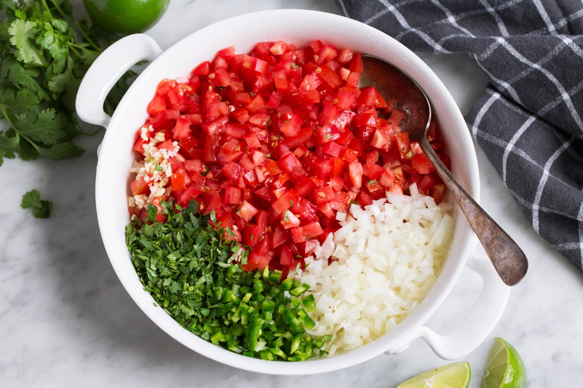 Showing how to make pico de gallo, mixing chopped tomato, onion, jalapeno, cilantro, garlic, lime and salt in a mixing bowl.