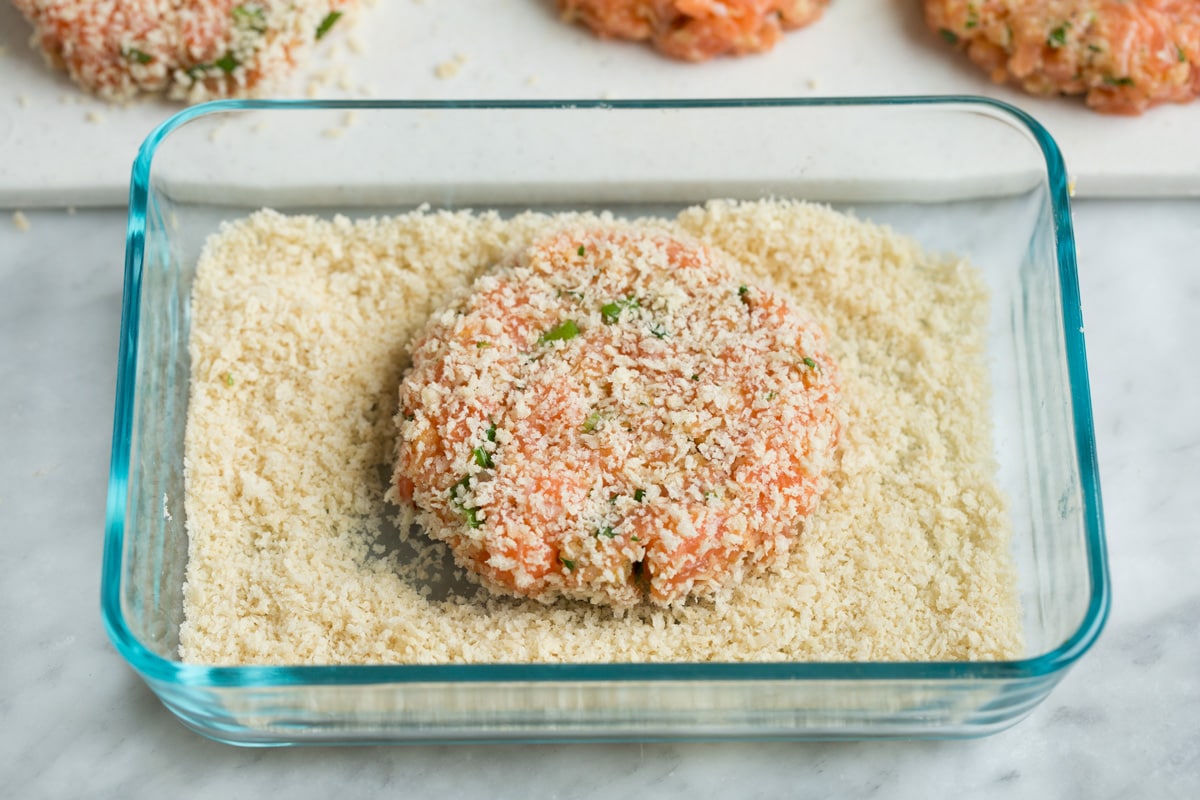Salmon patty dredged in panko in a small rectangular glass dish.