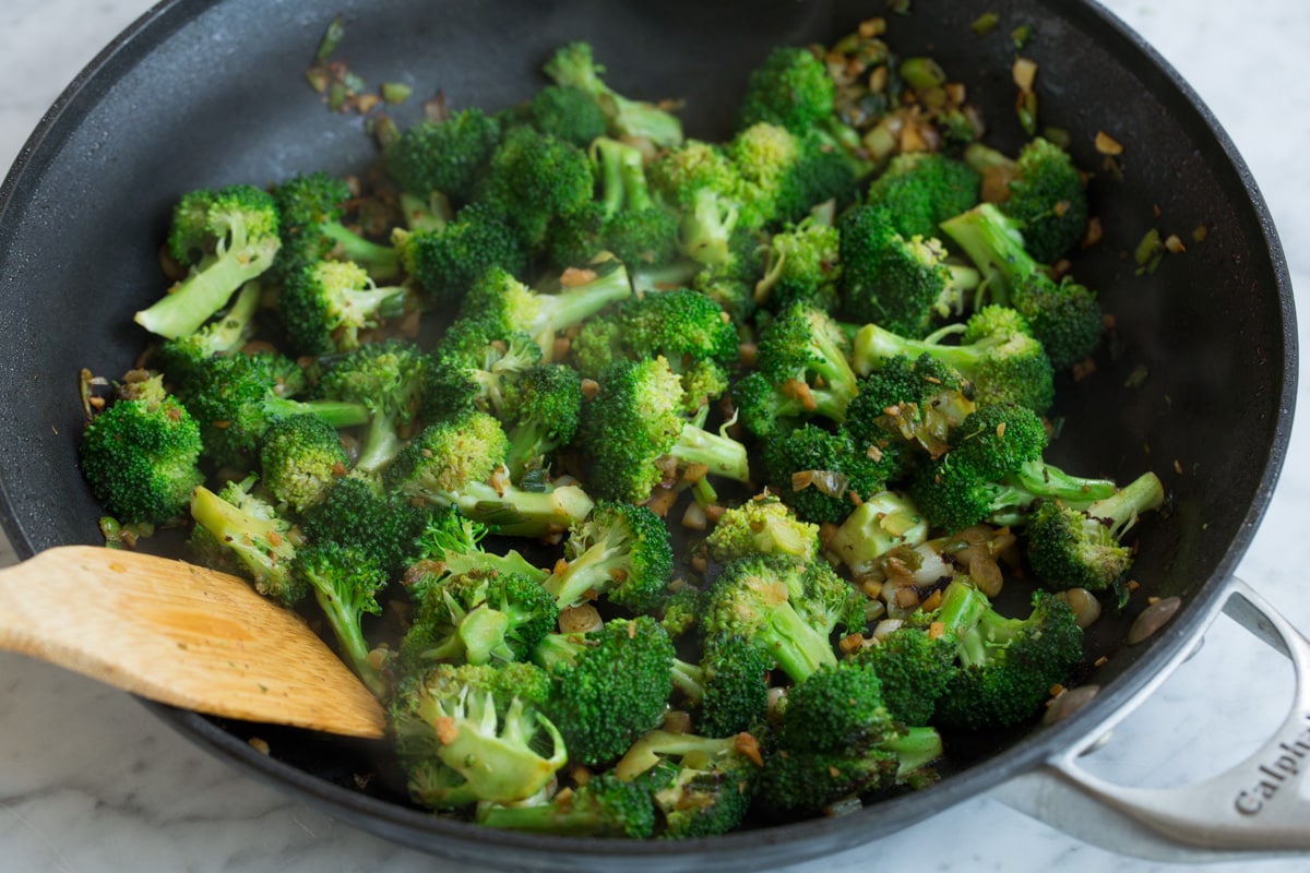 Cooking broccoli, onions and garlic in a skillet to make beef and broccoli.