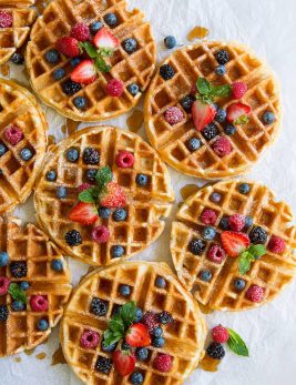 Eight Belgian Waffles topped with berries and maple syrup.