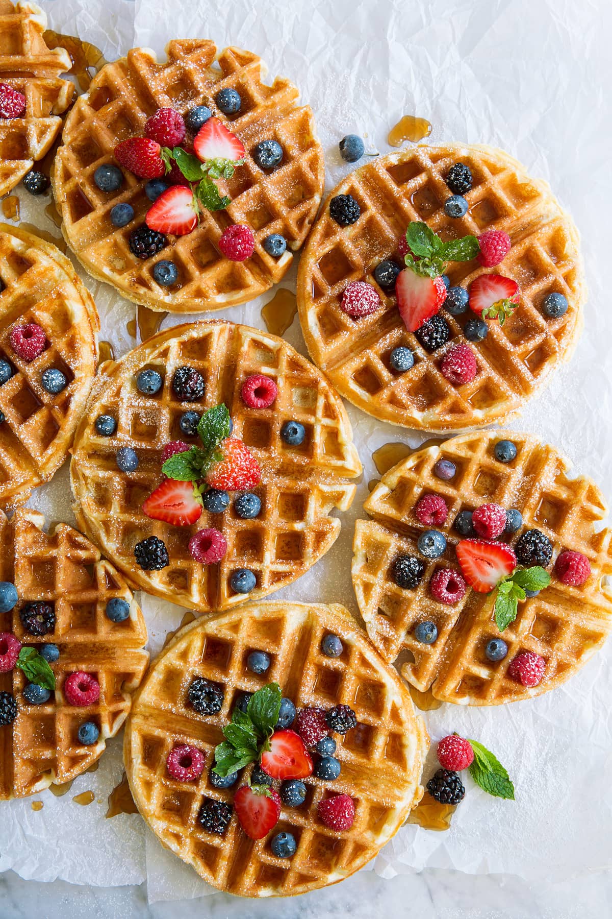 Eight Belgian Waffles topped with berries and maple syrup.