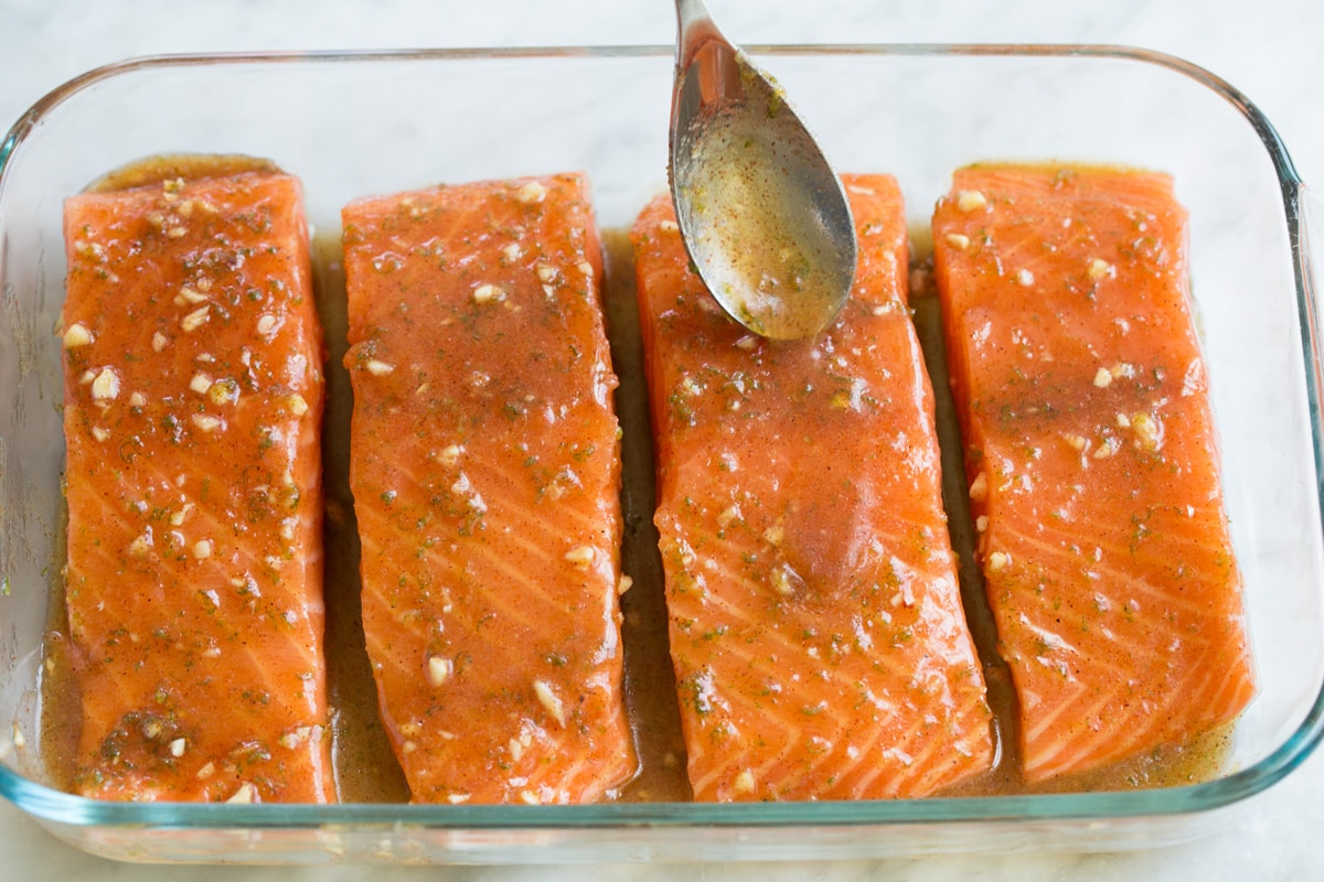Spooning sauce over salmon fillets in a small glass baking dish.