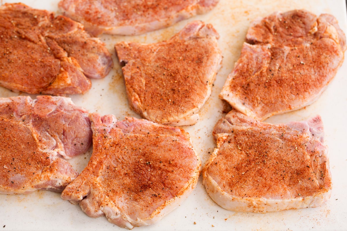 seven pork chops on a cutting board with dry rub