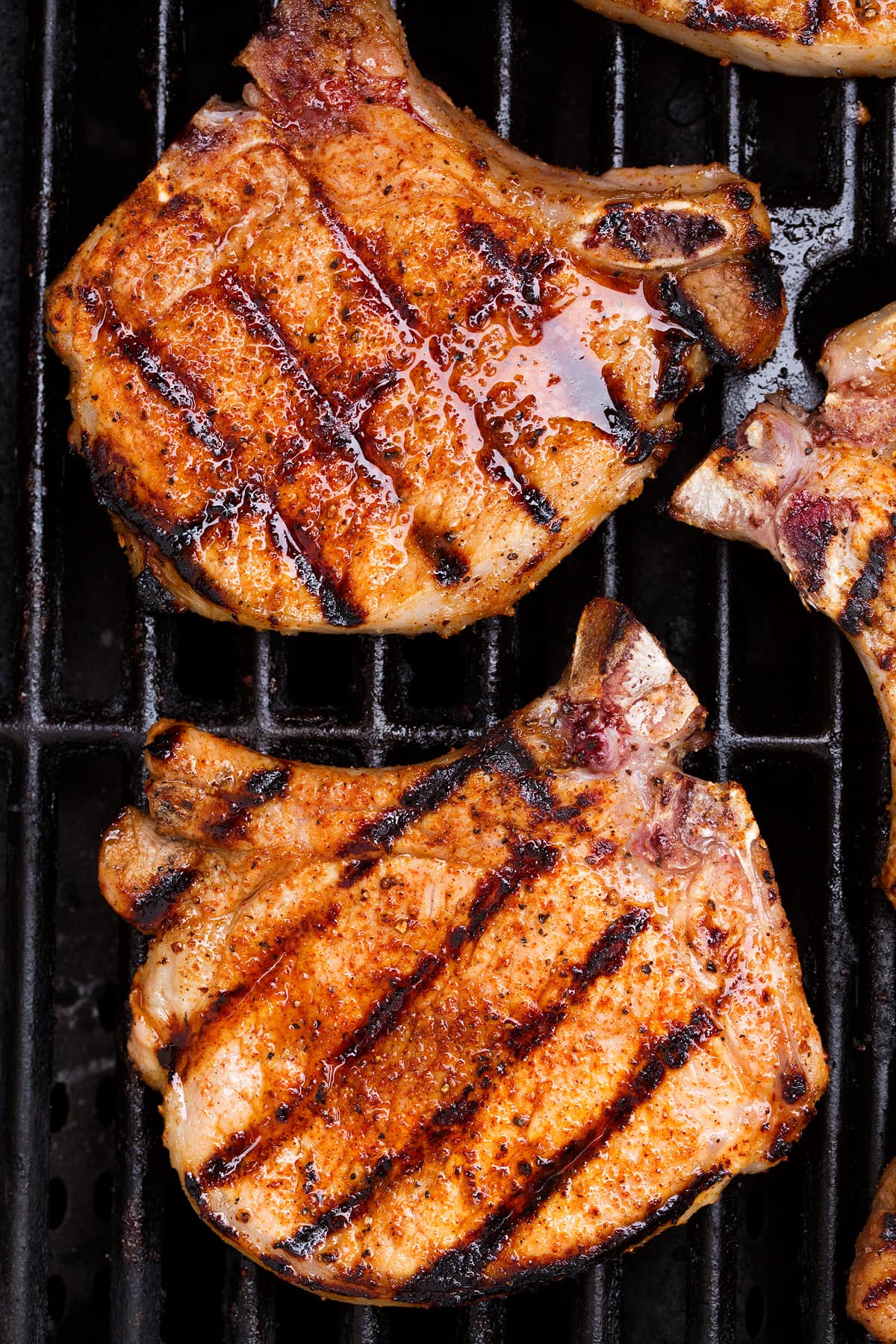 Overhead close up image of two pork chops on a grill.