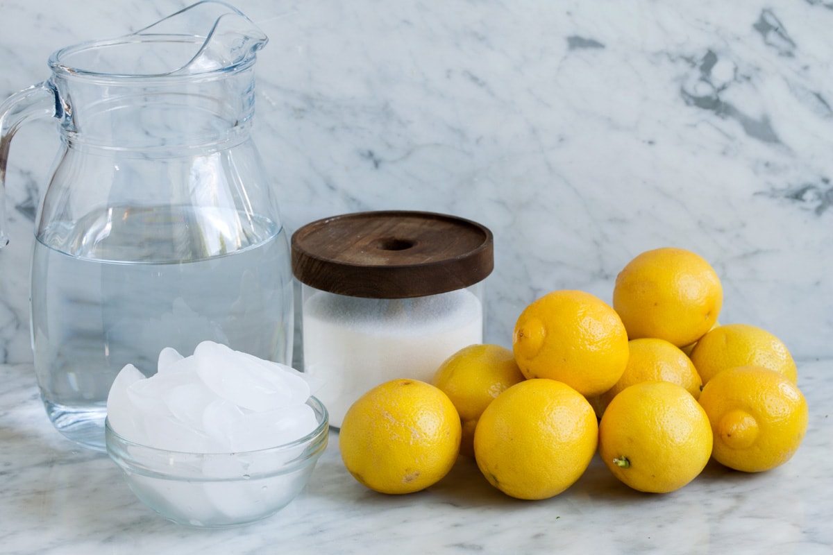 Ingredients to make lemonade, including fresh lemons, sugar, ice and water.