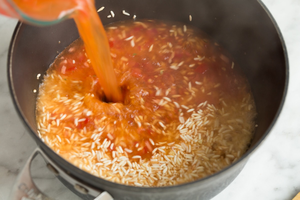 Adding liquid mixture to sautéed rice in saucepan.