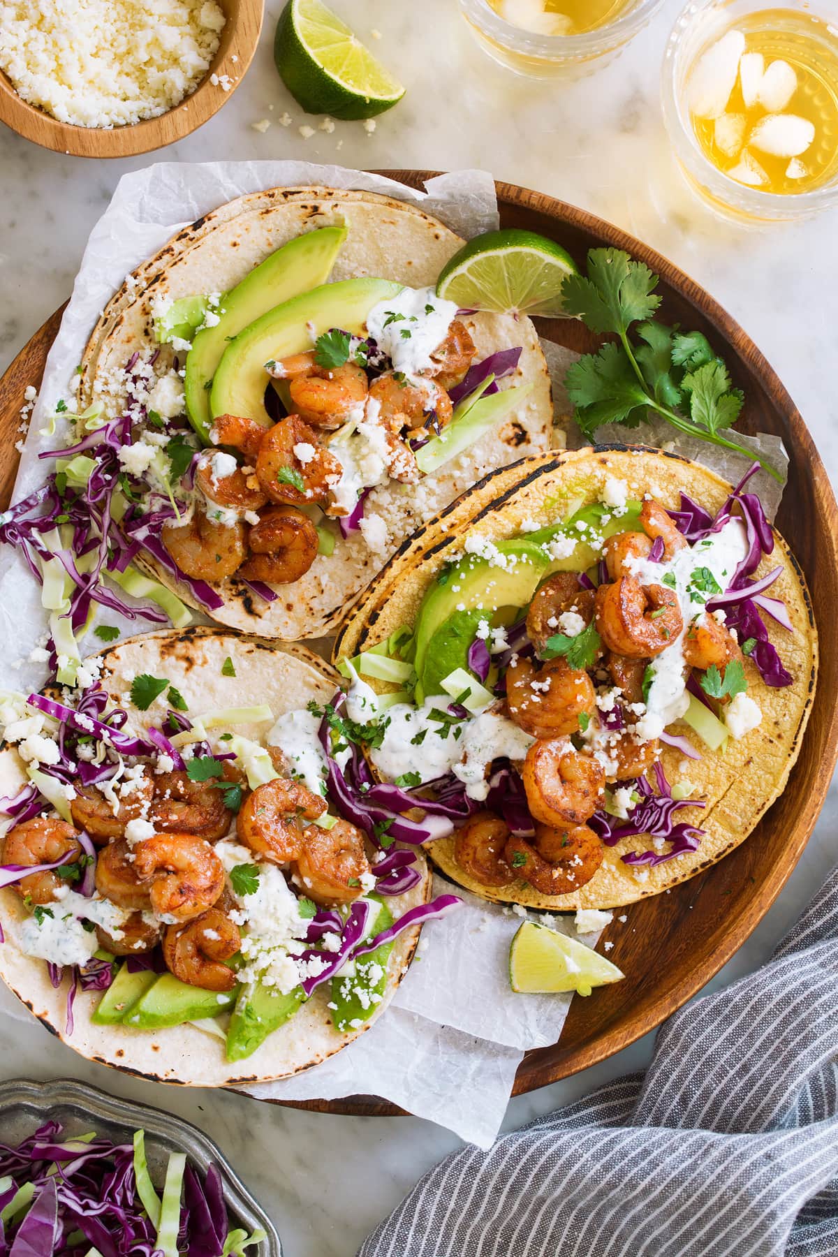 Shrimp Tacos on a wooden serving plate on parchment. Tacos are topped with cabbage, avocado, and cilantro lime crema.