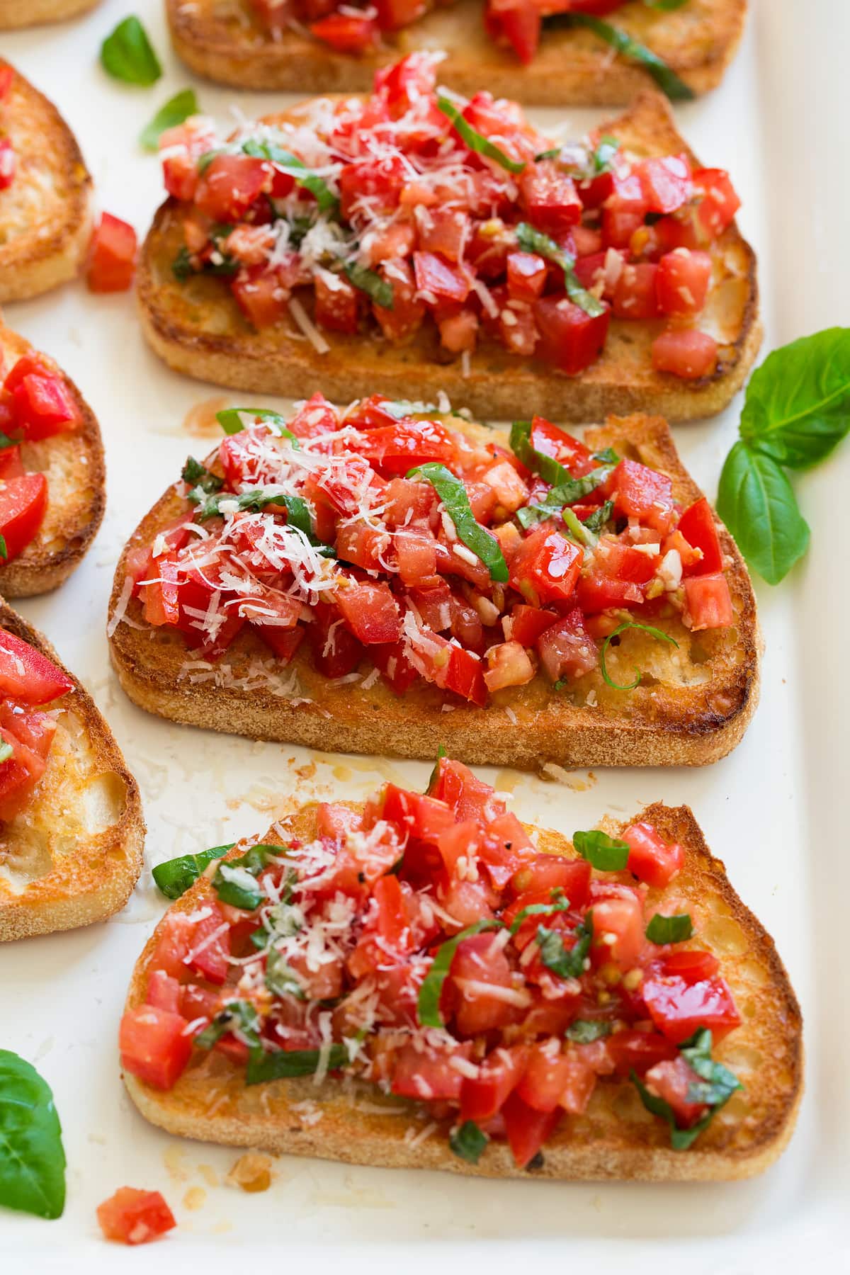 Bruschetta with toasted bread and fresh tomato basil mixture on top, set on a white serving platter.