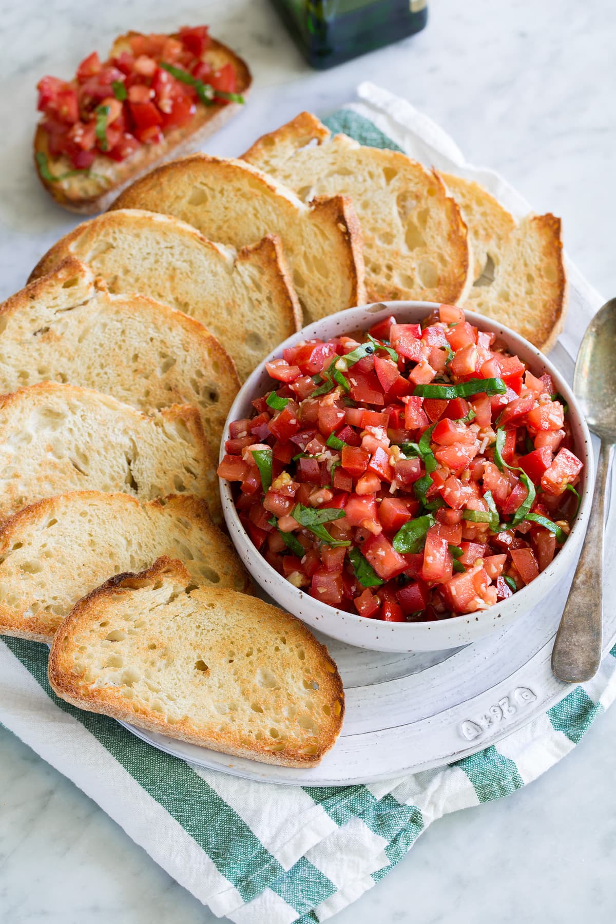 Tomato Bruschetta topping in a white serving bowl with toasted French bread on the side