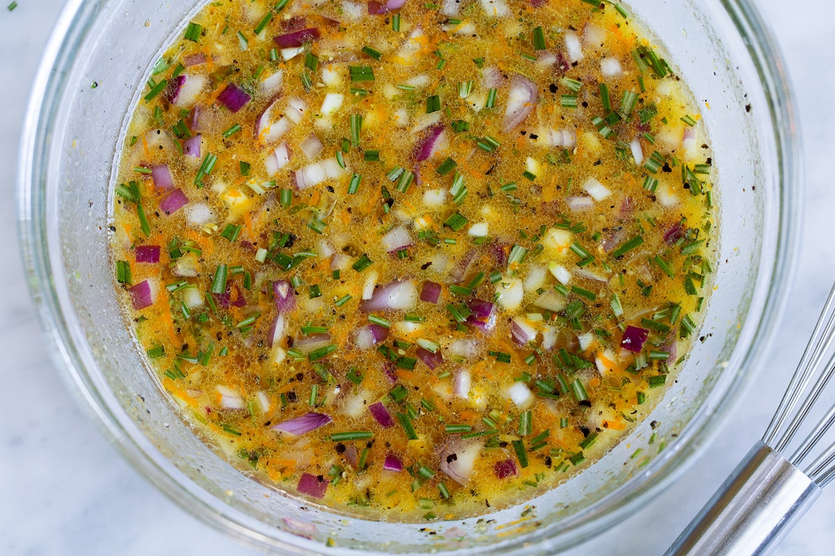 Chicken marinade in a glass mixing bowl. Made with citrus, olive oil, herbs, garlic and red onion.